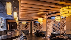 Zona de bar con mostrador curvo, asientos de cuero negro e iluminación cálida.