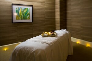 Un cuarto de spa con una camilla de masaje, velas y una obra de arte enmarcada en la pared.