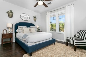 A bedroom with a bed, a chair, a window, and decorative wall art.