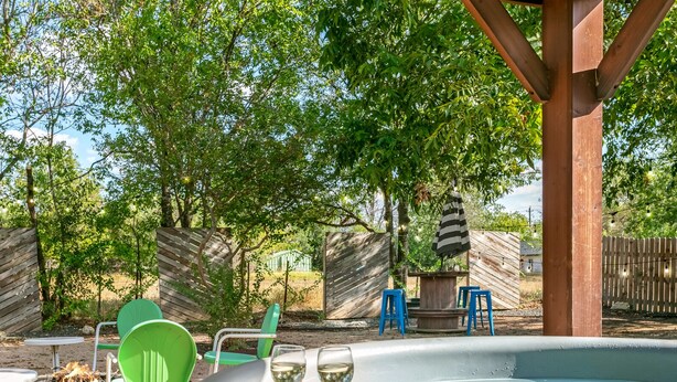 A hot tub with two glasses of white wine, surrounded by outdoor furniture and a wooden pergola. - Frieden Haus | 2/1, Hot Tub, Fire-pit, Full Kitchen (Fredericksburg)