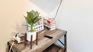 A flat-screen TV mounted on a wall above a wooden console table with a potted plant, books, and a remote control.