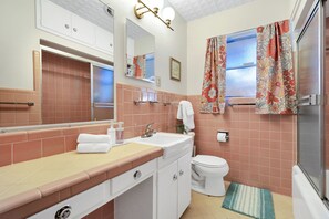 A bathroom with a sink, mirror, toilet, and shower area.