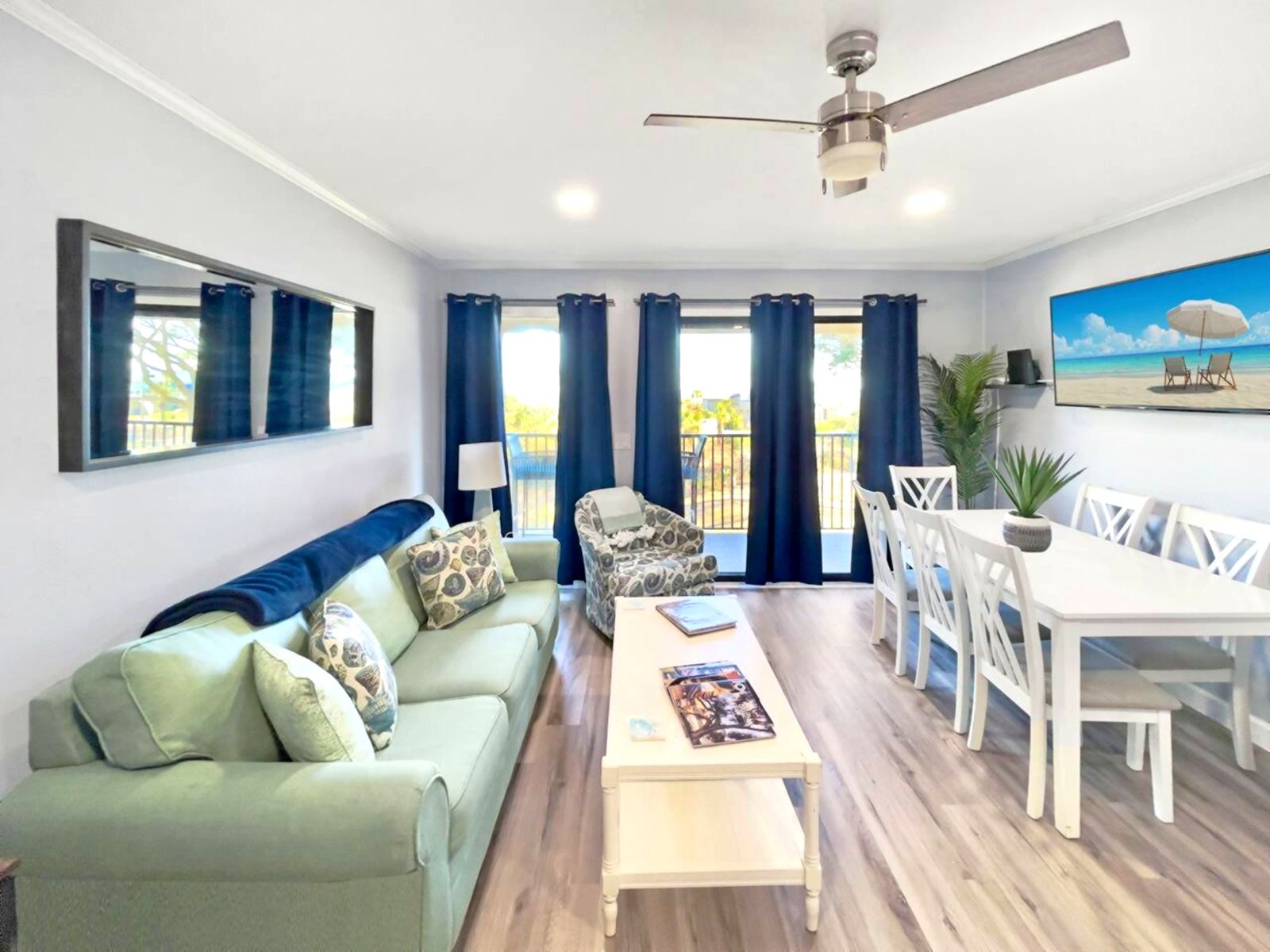 Un salon comprenant un canapé, une table basse, une table à manger avec des chaises, un ventilateur de plafond et une vue sur l’extérieur grâce à de grandes fenêtres.