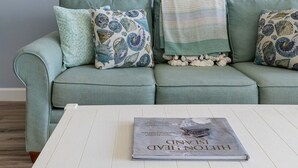 Una sala de estar con un sofá azul claro, cojines estampados, una mesa de centro blanca y un cuadro de una escena de playa.