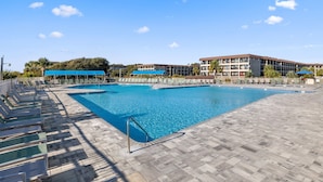 Una amplia piscina al aire libre con tumbonas y sombrillas, rodeada por un edificio de varios pisos y balcones.