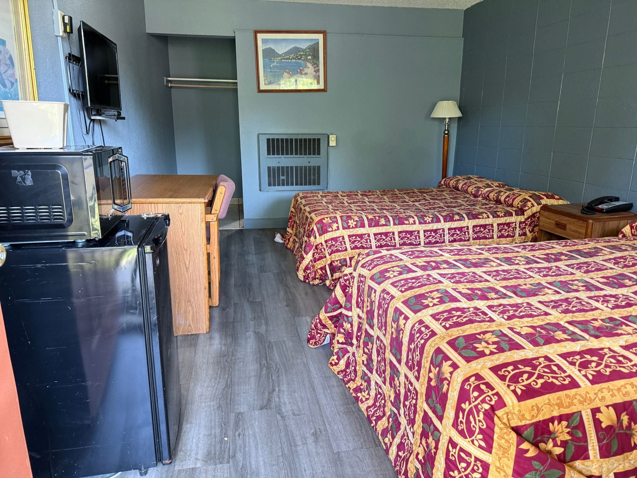 A hotel room with two beds, a desk, a television, and a picture on the wall.