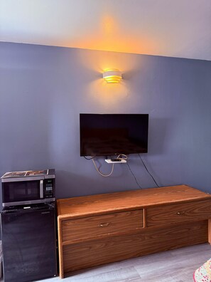 A room with a flat-screen TV mounted on the wall, a microwave, and a wooden dresser. - Clayton House Motel (Loves Park)