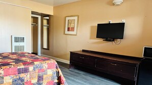 A bedroom with a large bed, a dresser, a TV mounted on the wall, and a framed picture. - Clayton House Motel (Loves Park)