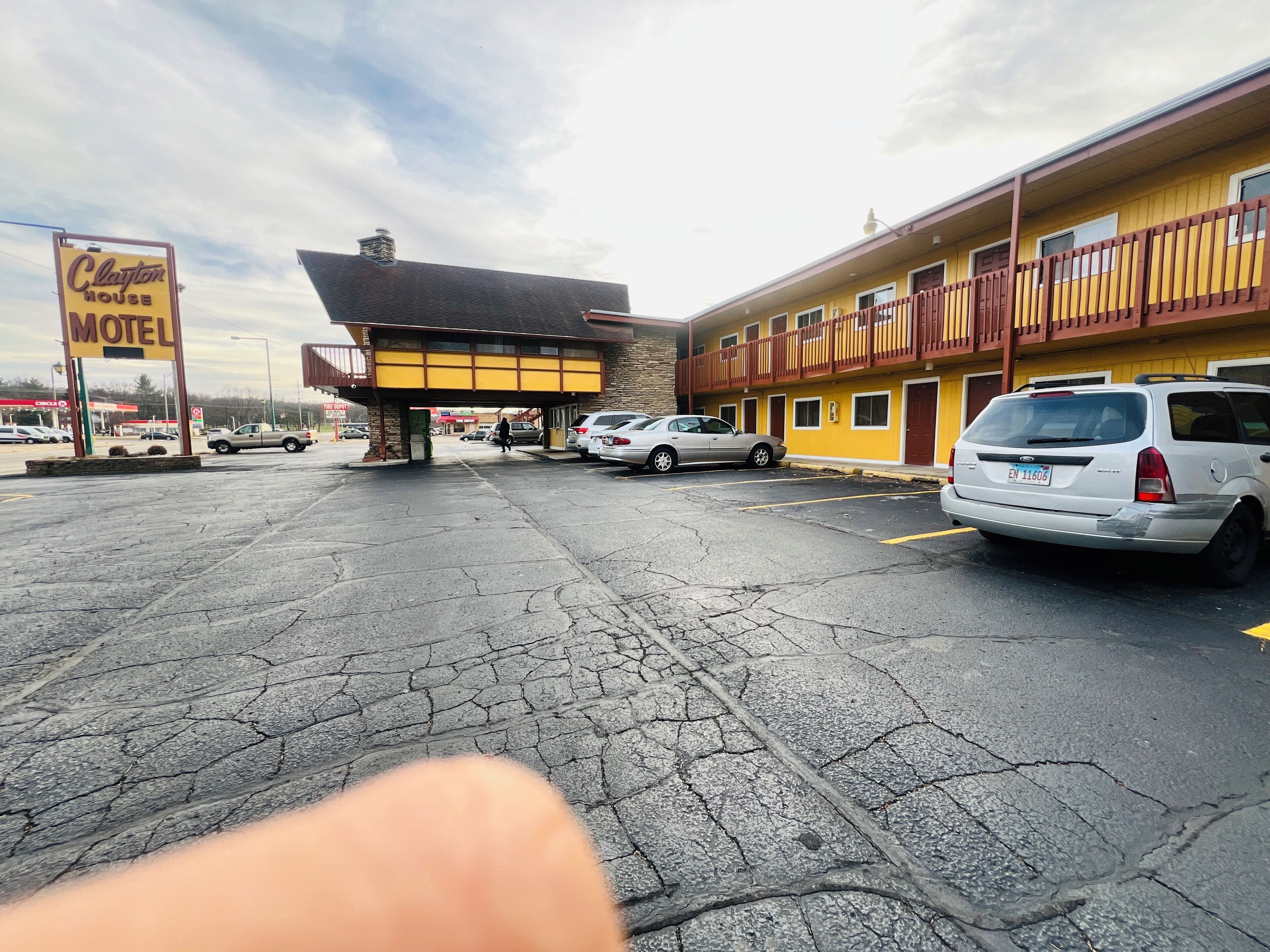 Een motel met een gele gevel, een overdekte parkeerplaats en een zichtbaar bord met de naam Clayton Motel.