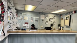 A reception desk with a white Christmas tree, various notices, and decorative wall art. - Clayton House Motel (Loves Park)