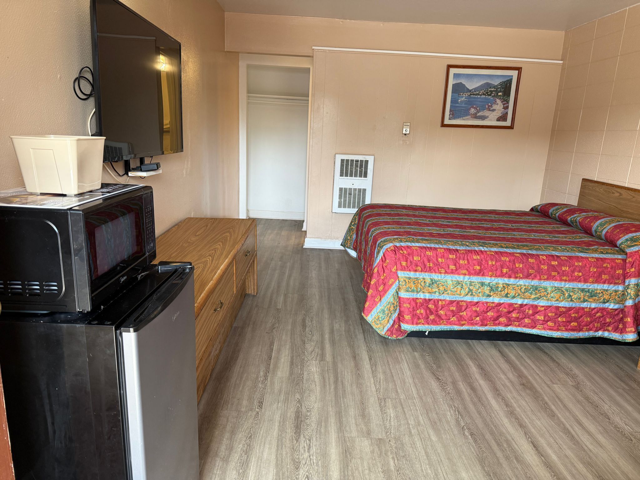 A compact hotel room with a bed, a wooden bench, a microwave, and a small kitchenette.