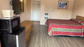 A compact hotel room with a bed, a wooden bench, a microwave, and a small kitchenette.
