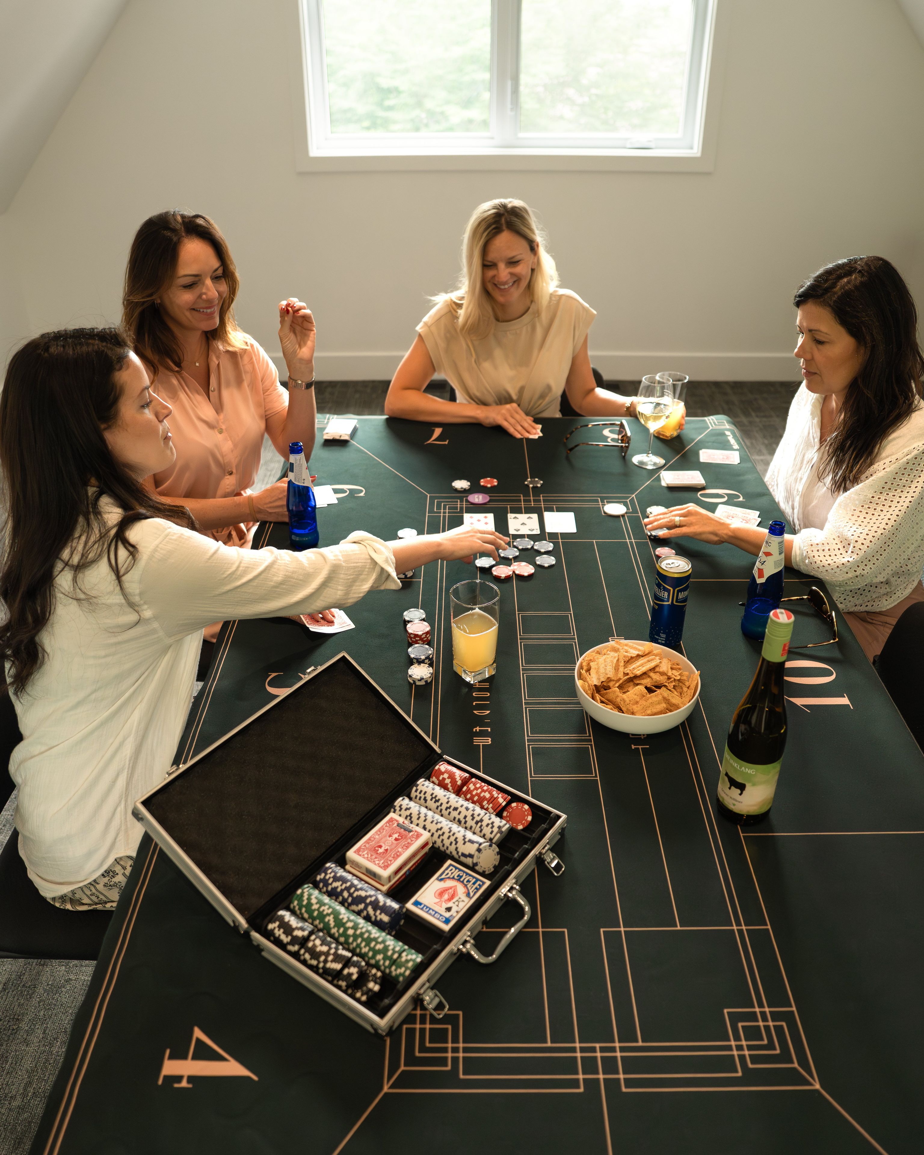 A group of people playing blackjack at a casino table with chips, cards, and drinks.