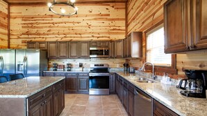 Una cocina amplia con paneles de madera, encimeras de granito y electrodomésticos de acero inoxidable, e una isla grande con asientos.