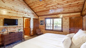 Un dormitorio tipo cabaña de madera con cama, cómoda, televisor y ventana con persianas.