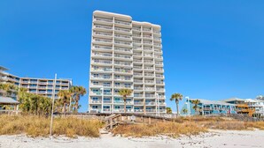 A beachfront hotel with multiple balconies, a wooden walkway, and palm trees.
