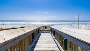 A wooden boardwalk leading to a beach with clear skies and ocean views.