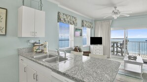 A kitchen with granite countertops, white cabinetry, a built-in sink, and a ceiling fan.