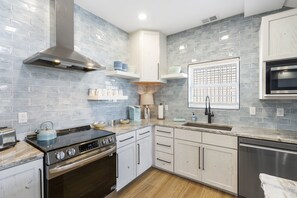 Une cuisine moderne équipée d’une cuisinière, d’un four, d’un four à micro-ondes et d’un lave-vaisselle. Les murs sont recouverts de carreaux bleu clair, les armoires sont blanches et le plan de travail est en bois.