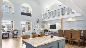 A spacious living area with a high ceiling, a marble island, and a dining set. - Restful Getaway with Boat Parking, Hot Tub, Free Attraction Tickets & 1 Mile to State Park Marina (Branson)