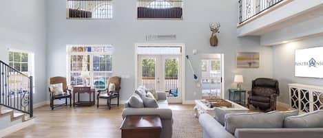 A spacious living area with a high ceiling, a staircase, and a balcony with a railing.