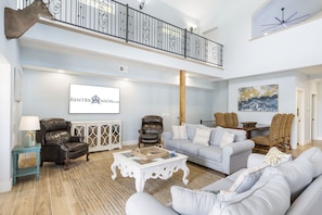 Un salon spacieux avec un plafond haut, un balcon doté d’une balustrade et une tête de cerf fixée au mur.