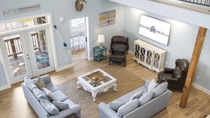 A spacious living room with a light blue sofa, a leather armchair, and a coffee table. There is a large window with a view of the outdoors, a door leading to a balcony, and a sign on the wall. - Restful Getaway with Boat Parking, Hot Tub, Free Attraction Tickets & 1 Mile to State Park Marina (Branson)