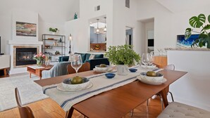 Ein geräumiges Wohnzimmer mit Kamin, Essbereich mit Holztisch, gedeckt für eine Mahlzeit, und eine große Pflanze.