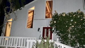 Uma casa com duas janelas visíveis, uma porta vermelha e um corrimão de varanda branco.