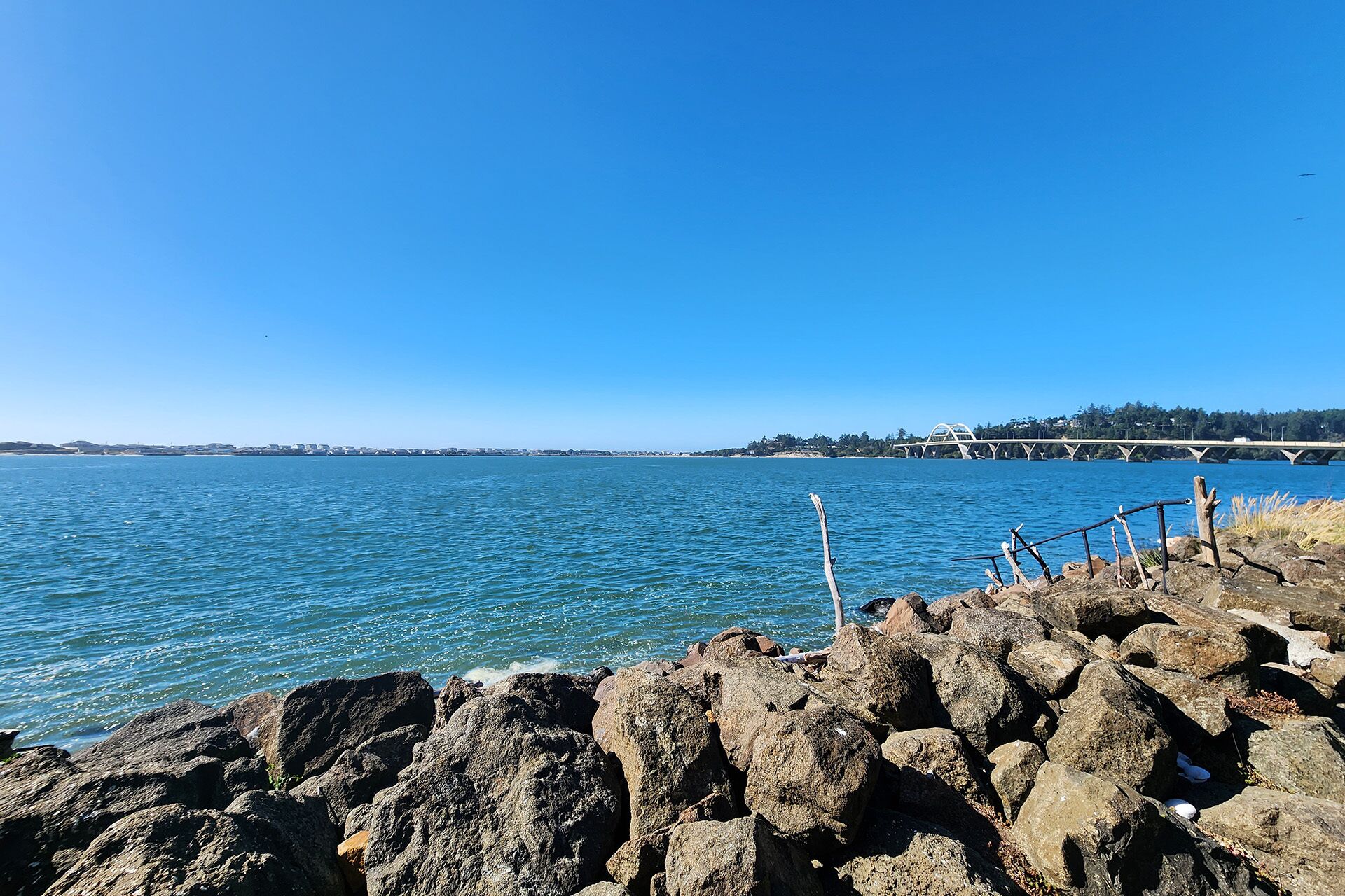 A rocky shoreline with a clear view of the water and a bridge in the distance.