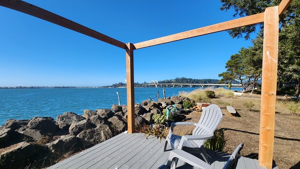 A wooden deck with a view of the water and a bridge in the distance.