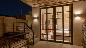 A modern outdoor patio with a wooden staircase, a glass door leading to a bedroom, and a stone wall. - Casa Antal  -  Yucatan Home Rentals (Mérida)