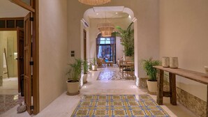 A hotel hallway with a patterned floor, potted plants, a wooden bench, and a chandelier. - Casa Antal  -  Yucatan Home Rentals (Mérida)