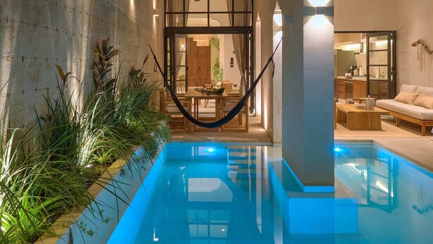 A modern pool area with a hammock, a dining area, and a seating area with a sofa. - Casa Antal  -  Yucatan Home Rentals (Mérida)