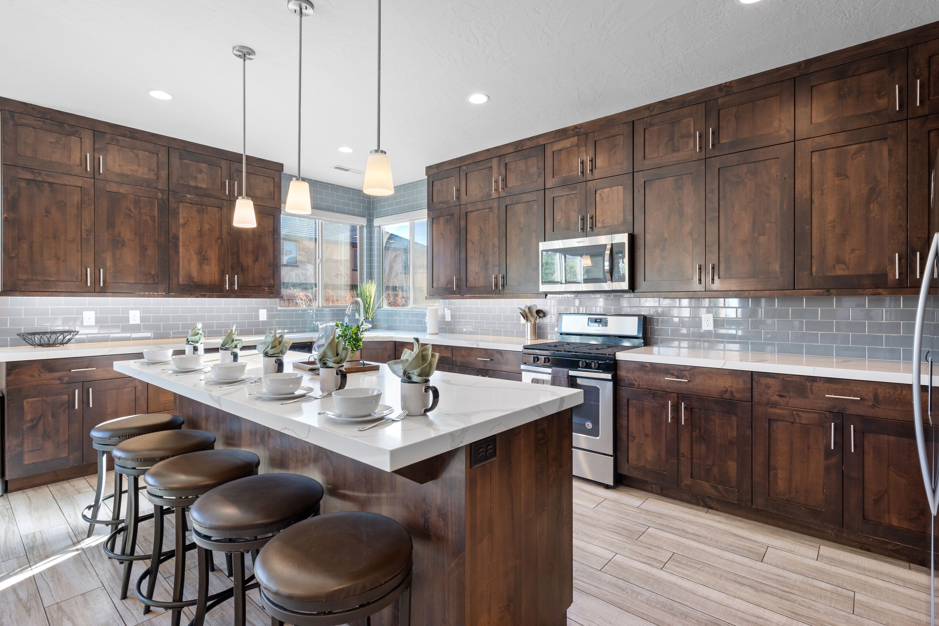A modern kitchen with dark wooden cabinets, a large island with stools, stainless steel appliances, and pendant lighting.