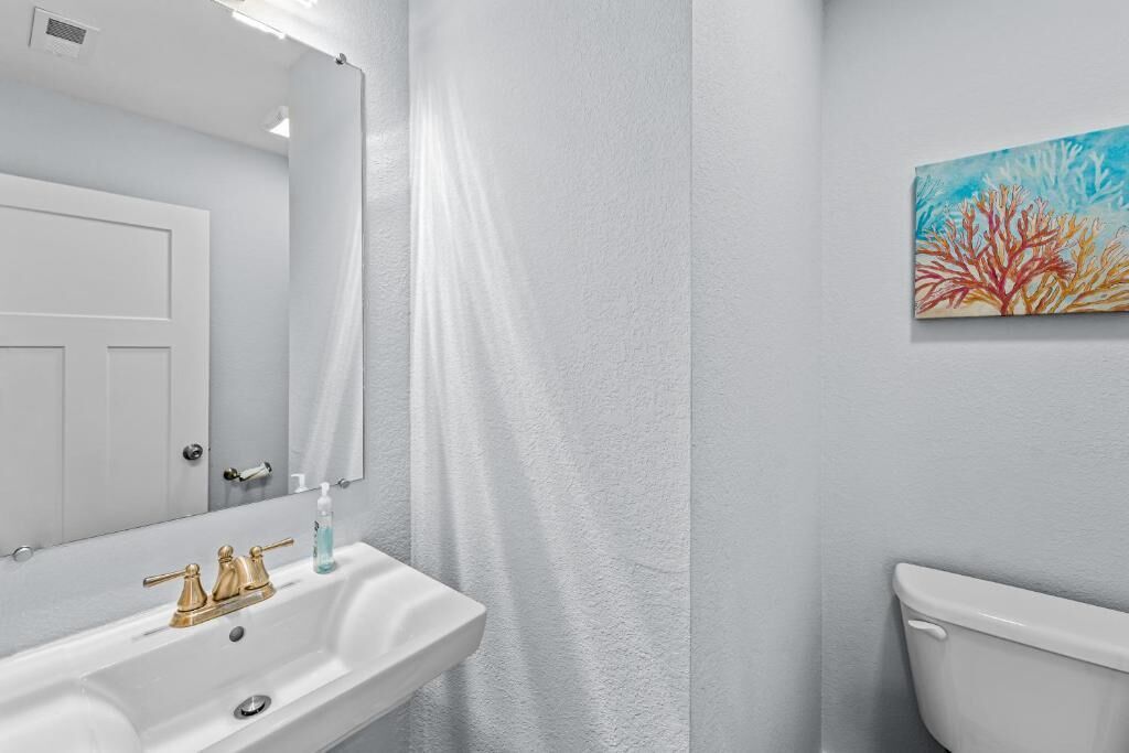 A bathroom with a white sink, gold faucets, a mirror, and a toilet.