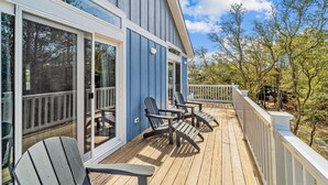 En træterrasse med Adirondack-stole, store vinduer og et hvidt gelænder.