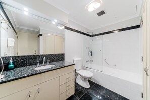 Een moderne badkamer met een granieten aanrechtblad, toilet, douche en een grote spiegel.