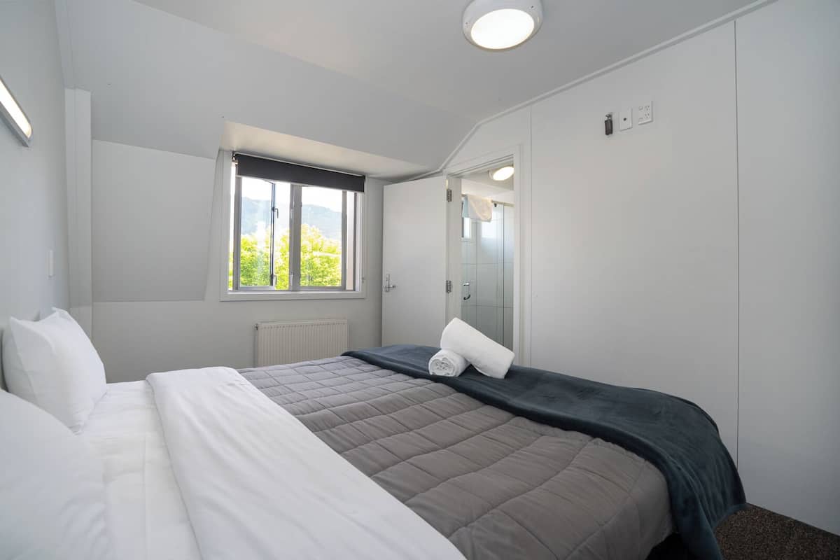 A bedroom with a bed, a window, a radiator, and a mirror.