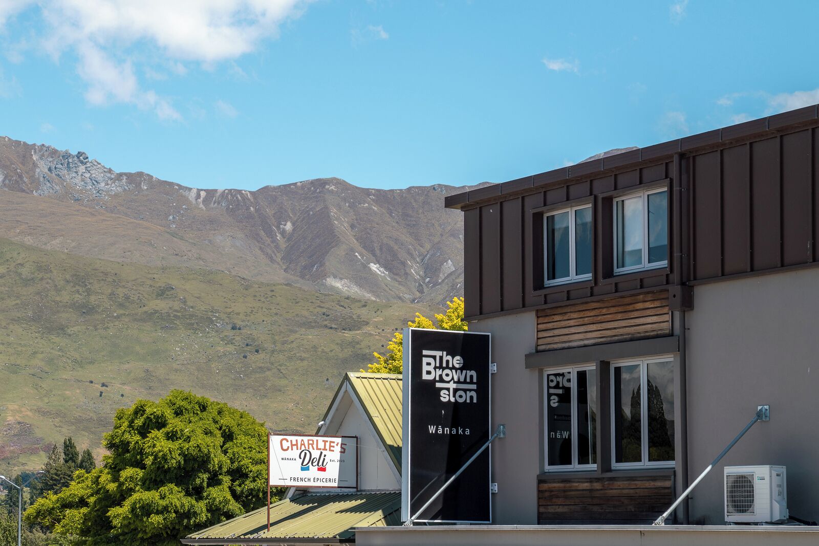 Un edificio con insegne per "The Brown Ston" e "Charlie’s Deli", sullo sfondo montagne.