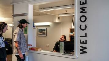 Uma receção com uma placa de 'WELCOME', um quadro na parede e uma pessoa sentada atrás do balcão.