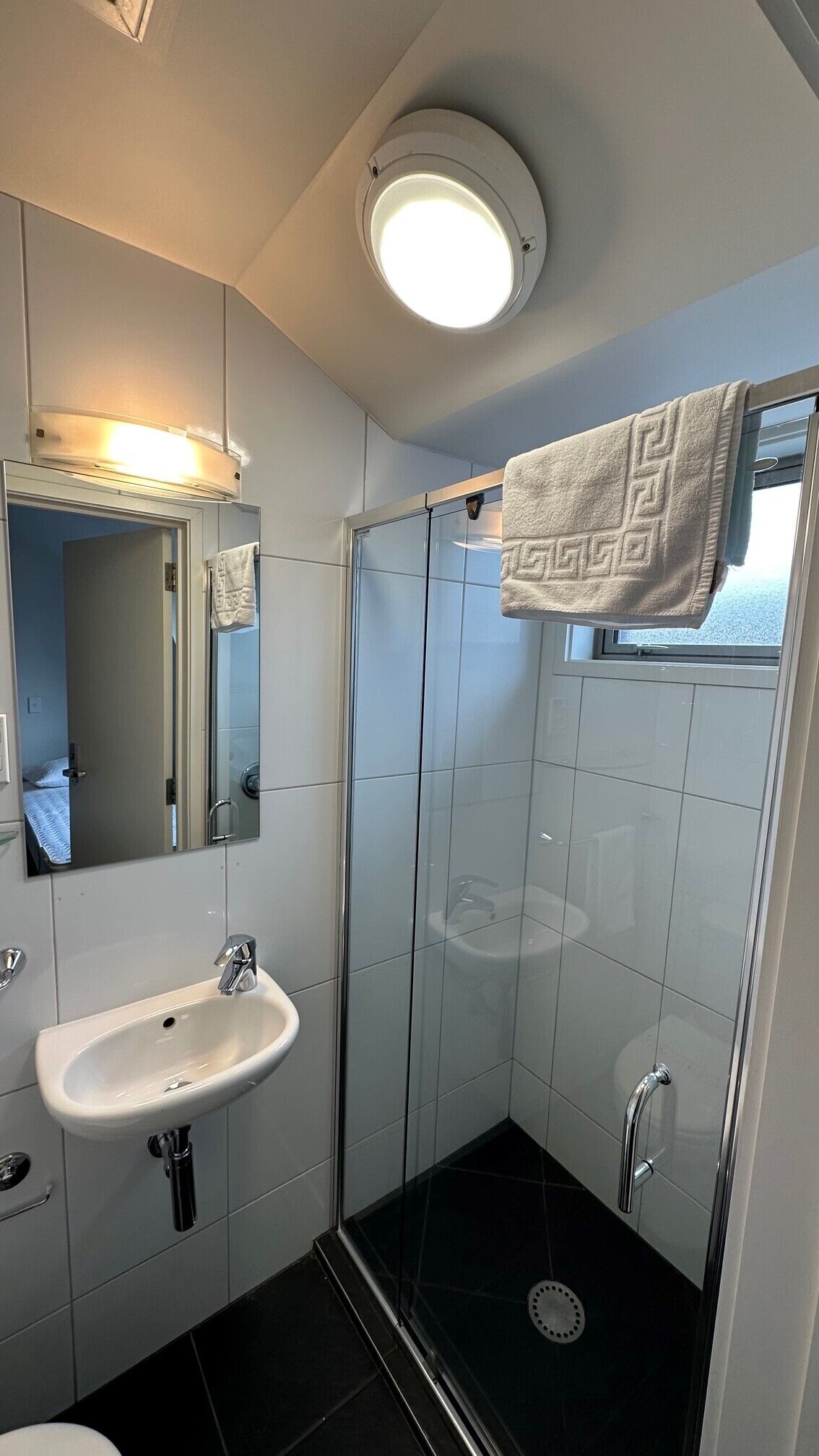 Un baño moderno con un lavamanos blanco, un espejo, una ducha con puerta de cristal y una toalla colgada en la pared.