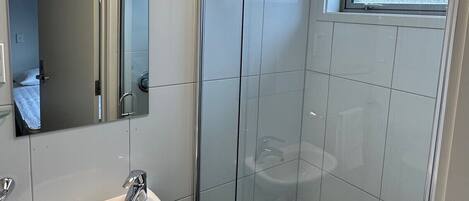 Un baño moderno con un lavamanos blanco, un espejo, una ducha con puerta de cristal y una toalla colgada en la pared.