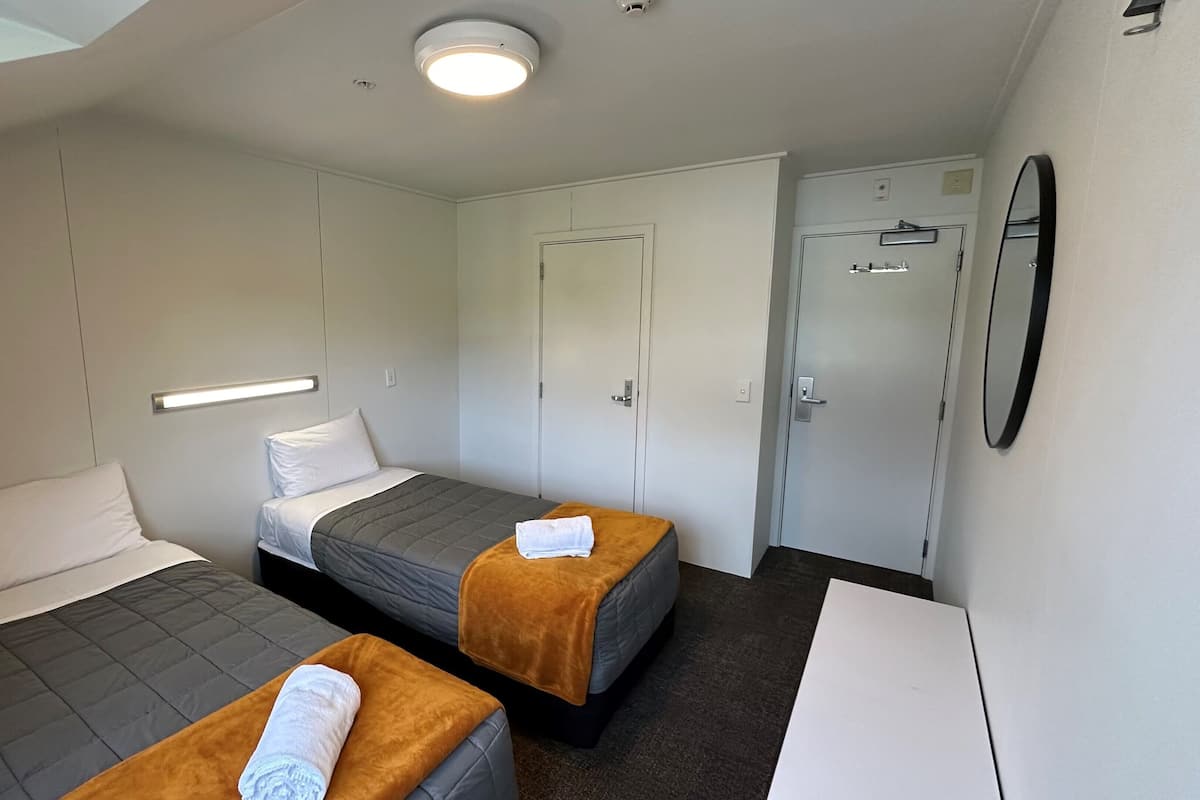 A small, modern hotel room with two beds, a desk, and a mirror.