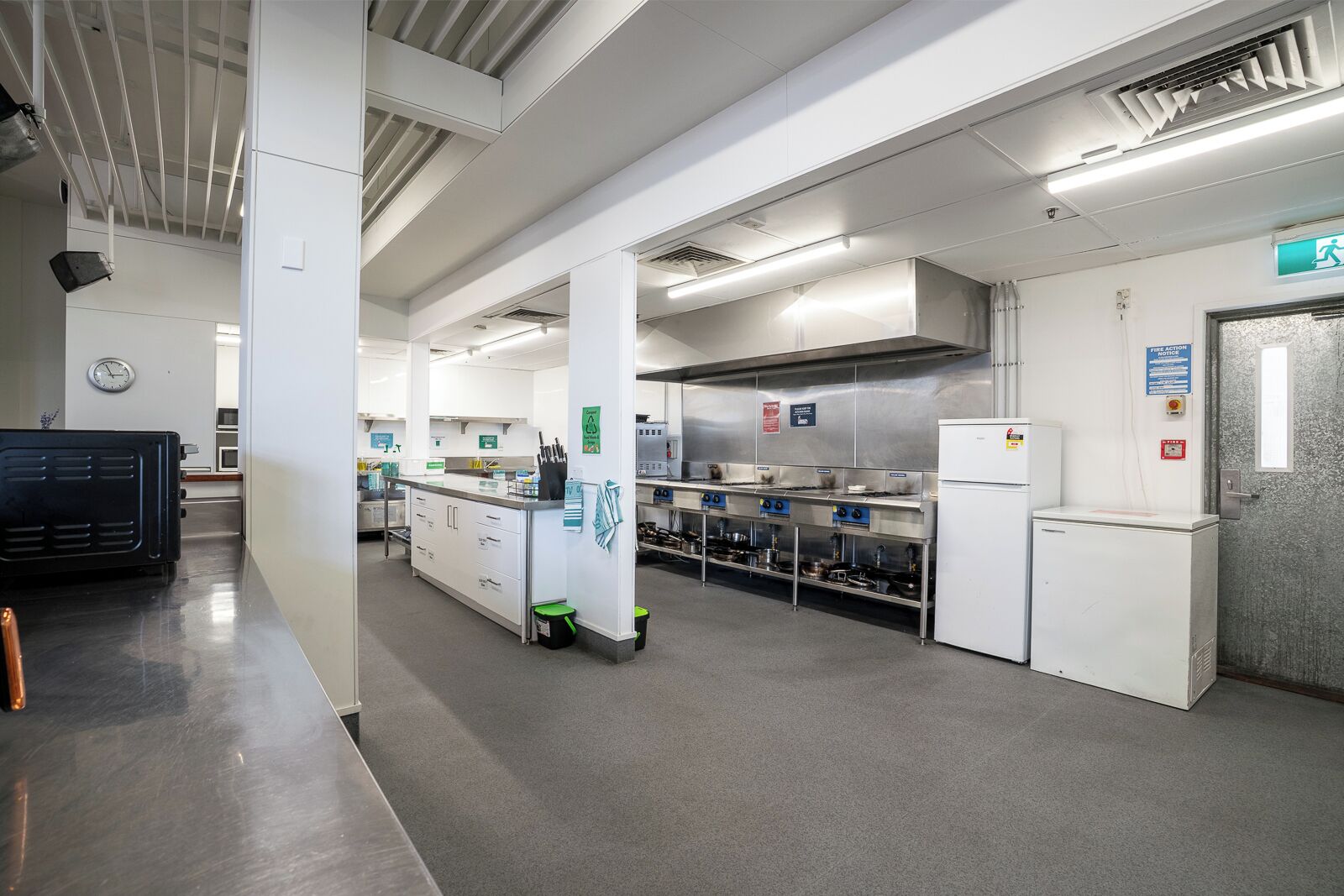 A spacious commercial kitchen with stainless steel appliances, a central island, and a fire action sign.