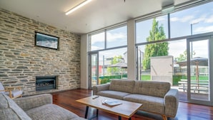 A spacious living area with a stone wall, a fireplace, a large window, and a modern sofa set. - The Brownston Hostel (Wanaka)