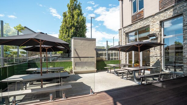 An outdoor patio with tables and umbrellas, stone walls, and a view of the surrounding area. - The Brownston Hostel (Wanaka)