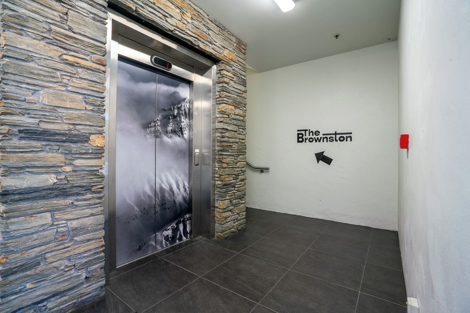 An elevator with a stone wall and a sign for "The Brownston".