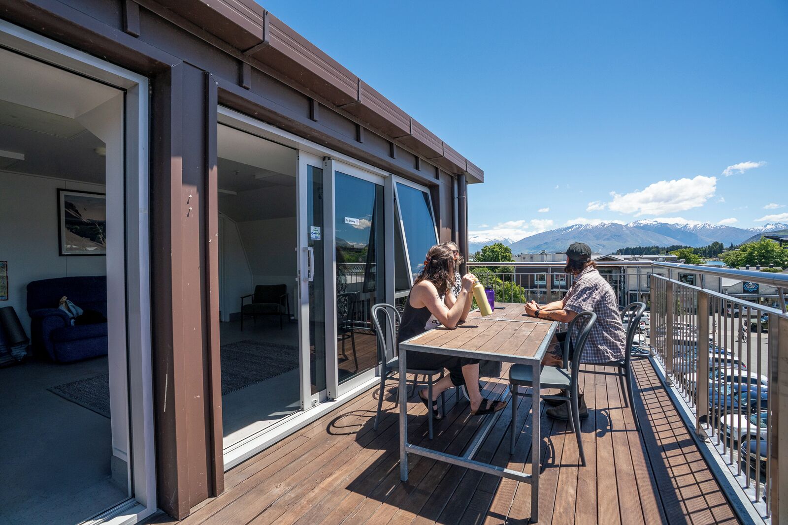 A deck with a table and chairs, a sliding glass door leading to an indoor area, and a view of mountains in the background.
