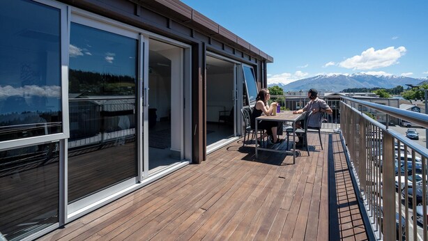 A deck with a wooden floor and glass doors leading to an interior space, overlooking a mountainous landscape. - The Brownston Hostel (Wanaka)